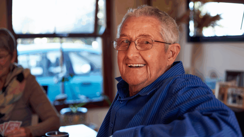 An old man with glasses and a blue shirt smiling back to the camera.