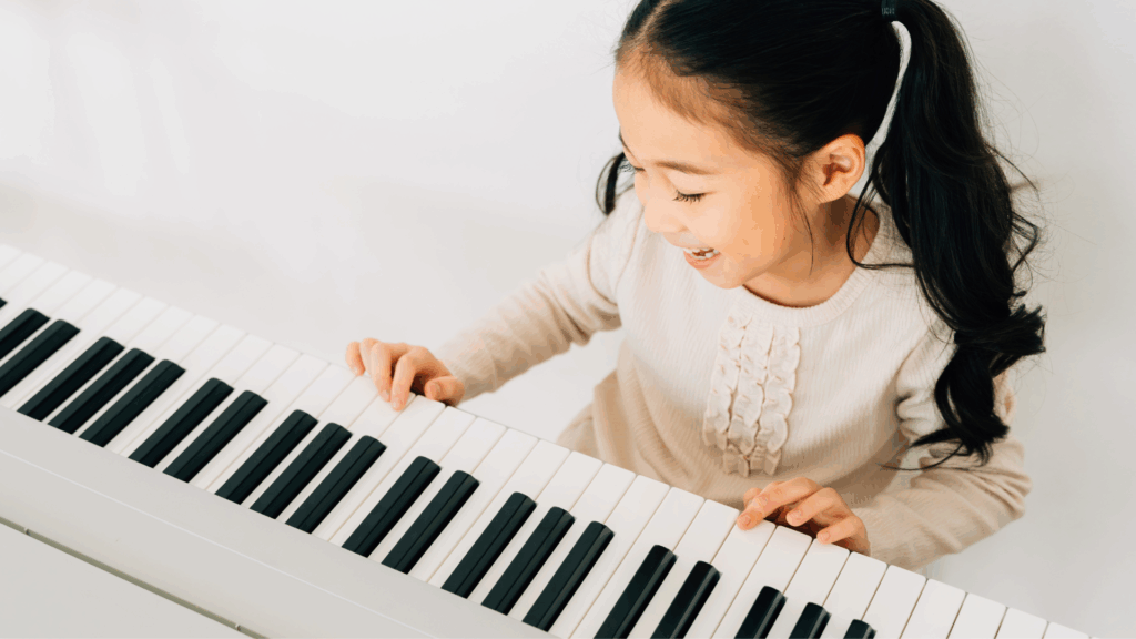 A young Asian girl playing the piano and smiling.